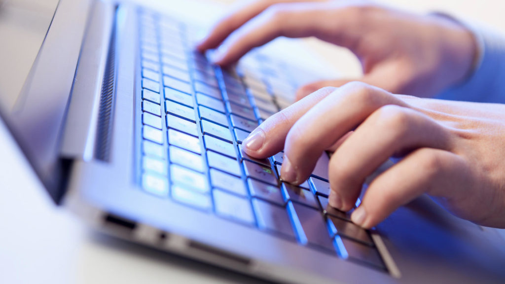 Click! Hands of a man on a keyboard with blue backlighting.